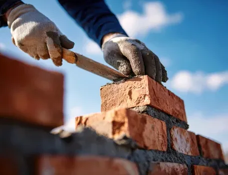 Mason laying new brick at the top of a chimney above the roofline